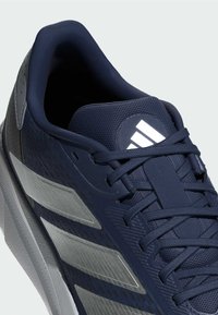 Scarpe sportive blu navy con tomaia testurizzata, dettagli grigi, logo a tre strisce e suola a contrasto. Design con lacci e colletto imbottito.