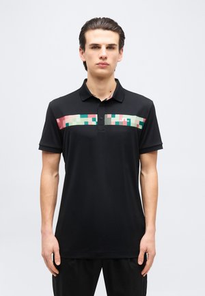 Giovane uomo con capelli tirati indietro che indossa una polo nera con un motivo geometrico rosa, verde e bianco sul petto.