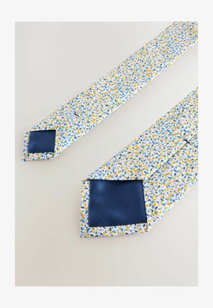 Cravatta in cotone con sfondo bianco e motivi di foglie blu e gialle, rifinita con una parte posteriore in satin blu scuro.