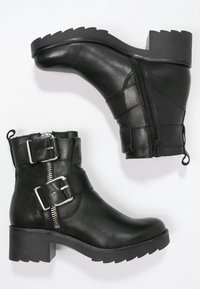 Svarta läderankelstövlar med en kraftig klack, siddragkedja och metallspännen. Texturerat ovanside med en robust sula.