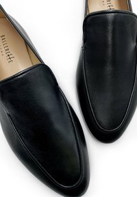 Black leather loafers with a sleek design, elongated shape, and subtle seam detailing. Smooth texture, minimal accents, and no visible hardware.