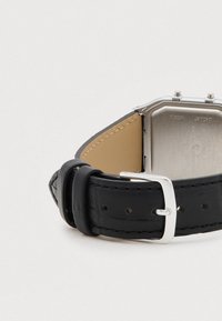 Juodas odinis laikrodis su sidabriniu nerūdijančio plieno korpusu ir metaliniais elementais. Dirželis turi lygų paviršių ir subtilius siūlus.