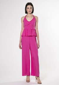 Roze haltertop met een peplum taille en uitsnijdingen, gecombineerd met wijde broekspijpen in dezelfde stof, afgemaakt met een paar sandaaltjes met banden.