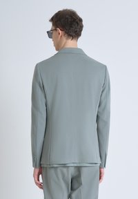 Blazer grigio realizzato in tessuto liscio, con una vestibilità su misura, rever a lancia e tre bottoni su ciascun polsino. Mostrato da dietro.