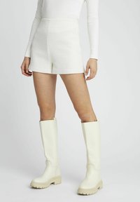 Shorts blancs texturés avec une taille haute et une finition lisse, associés à des bottes de pluie crème montantes avec une semelle crantée.