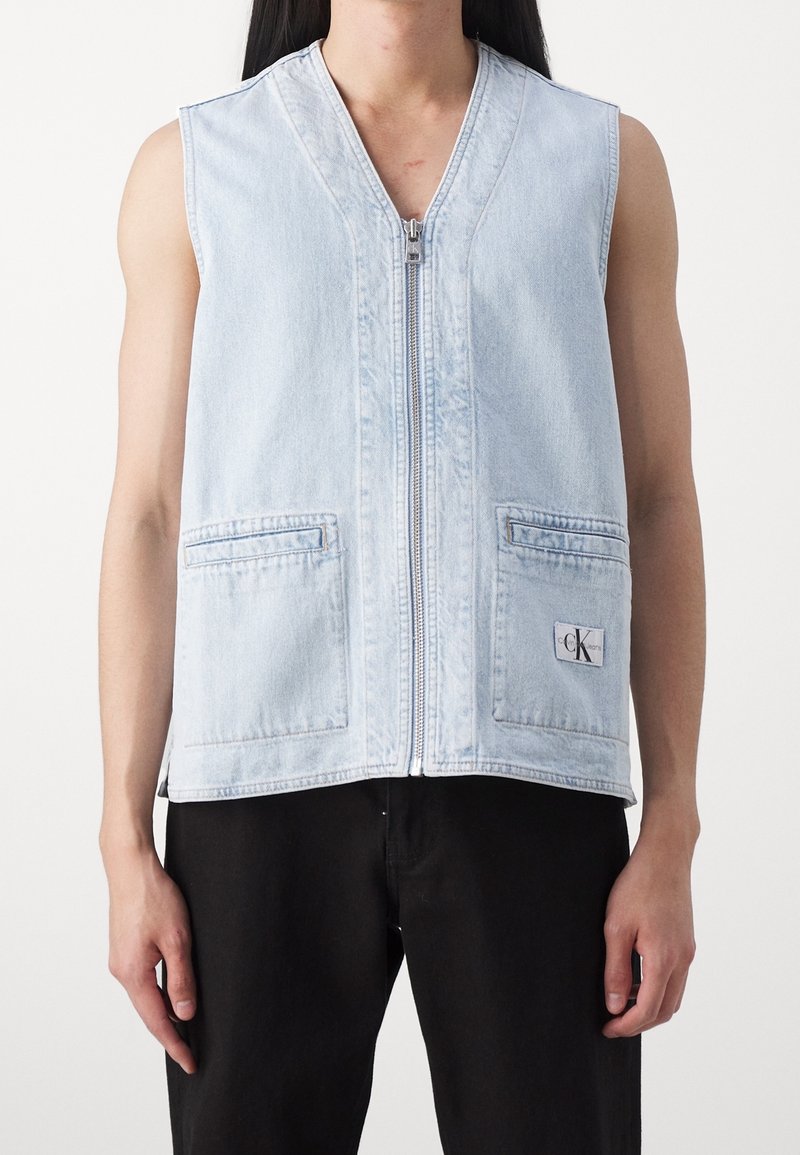 Světlomodrá džínová vesta se zapínáním na zip vpředu, dvěma předními kapsami a malou logovou nášivkou. Bez rukávů, volný střih.
