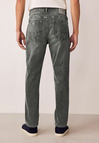Grey denim jeans with a relaxed fit, featuring two back pockets and a waistband tag. The material has a textured, slightly faded appearance.