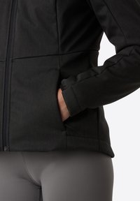 Svart jacka med texturerad tyg; har en hel dragkedja, sidofickor och åtsittande ärmar, i kombination med grå leggings.