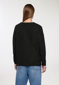 Czarny oversize sweter z okrągłym dekoltem, o miękkiej fakturze i długich rękawach, w zestawie z jasnoniebieskimi dżinsami.