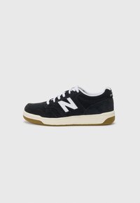 Svart semsket sneakers med hvite detaljer, inneholdende en fremtredende logo, hvite lisser og en gummisåle. Lavt design med teksturert overflate.