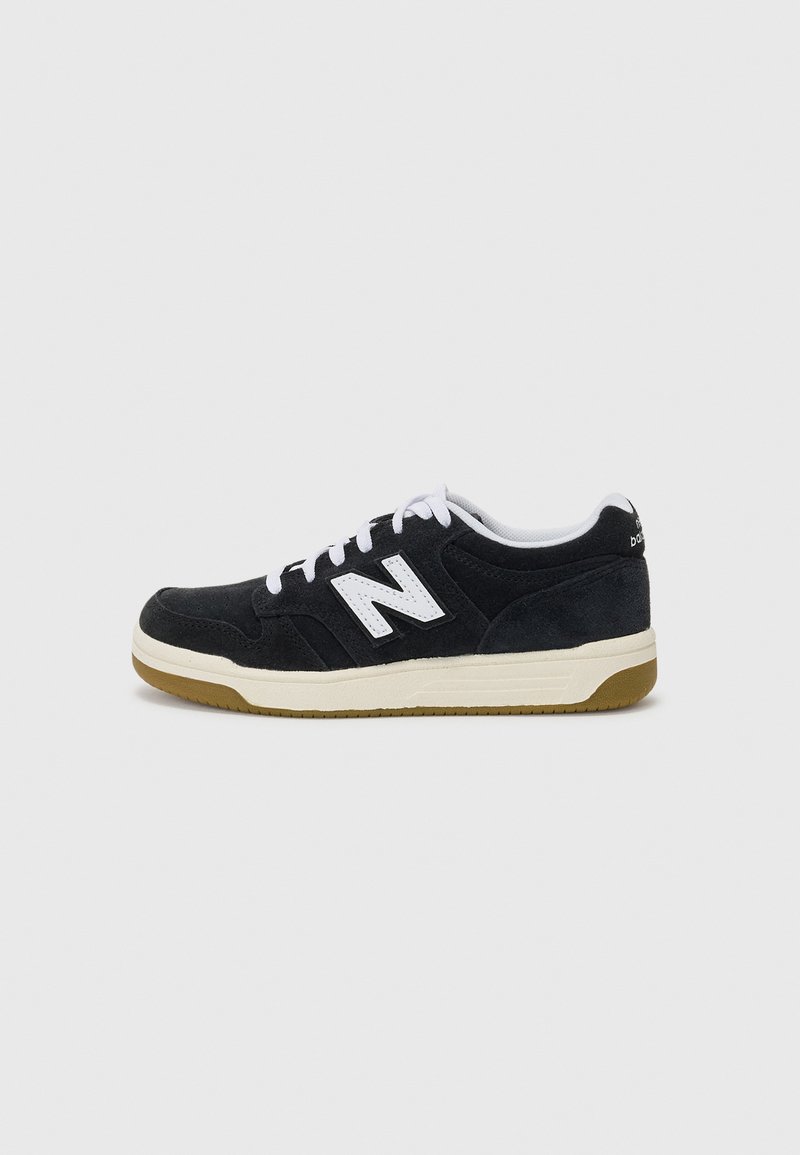 Svart semsket sneakers med hvite detaljer, inneholdende en fremtredende logo, hvite lisser og en gummisåle. Lavt design med teksturert overflate.