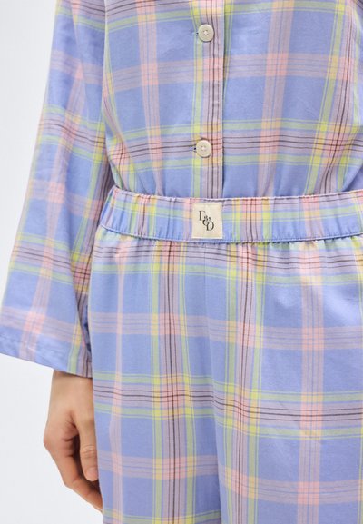 Κοντινό πλάνο ενός ατόμου που φοράει μπλε καρό πουκάμισο με κουμπιά και ταιριαστό παντελόνι με ελαστική μέση, με ριγέ σε παστέλ ροζ, πράσινο και κίτρινο.