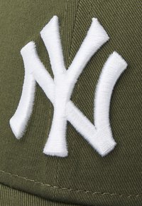 Olivgrüner Hut mit einem auffälligen weißen, gestickten "NY"-Logo. Der Stoff ist strukturiert und weist sichtbare Nähte auf.