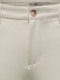 Gros plan sur la ceinture d'un pantalon beige avec une fermeture par bouton et une étiquette de marque "ONLY & SONS" visible à l'intérieur.