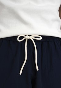 Cordon blanc noué en nœud sur une ceinture élastique marine, associé à un t-shirt blanc côtelé rentré.
