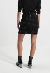 Mini-jupe noire à pois blancs, design ajusté, fermeture éclair arrière, associée à des bottines noires brillantes et un haut noir.