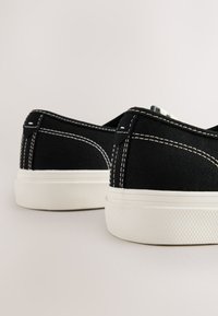 Sneakers nere in tela con cuciture bianche, punta tonda e suola in gomma texturizzata; design basso con finitura liscia e accenti sottili.