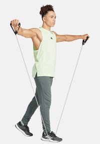Abbigliamento fitness con una canotta senza maniche verde chiaro e pantaloni jogger grigio scuro, con bande elastiche e scarpe da ginnastica nere.