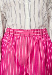 Pruhovaná košile na knoflíky v lehkém materiálu, spárovaná se světlými růžovými šortkami s vertikálními bílými pruhy a elastickým pasem.