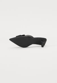 Chaussure noire à bout pointu avec un petit talon. Fabriquée en matériau lisse, dotée d'une semelle texturée. Accentuée par une petite boucle sur le dessus.