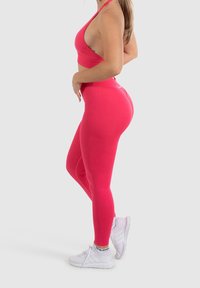 Sada aktivního oblečení na tělo v jasně růžové barvě, zahrnující crop top s křížovým zády a legíny s vysokým pasem. Texturovaná tkanina s plochými švy.