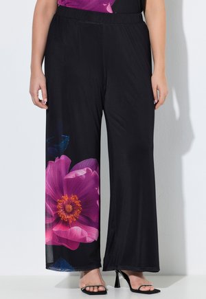 Sorte bukser med vide ben og stort pink blomsterprint på venstre ben, båret med sorte højhælede sandaler og en blomstret top.