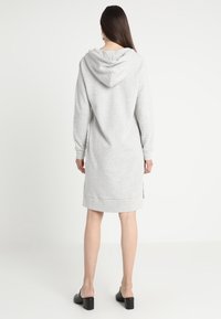 Graues Hoodie-Kleid mit langen Ärmeln, geripptem Saum und Kapuze. Leichte Seitenschlitze am Saum fördern die Bewegungsfreiheit. Glatte Stoffoberfläche.