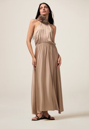 A long, beige satin halter dress with a ruffled neckline and an elastic waistband, complemented by strappy black sandals.