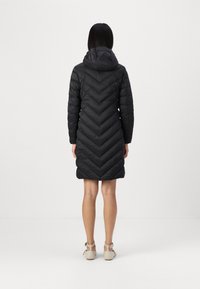 Abrigo acolchado negro con un diseño en forma de Chevron, que presenta una capucha y mangas largas, terminando por encima de las rodillas. Textura suave y material ligero.