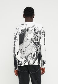 Πλεκτό πουλόβερ σε λευκό με μαύρο αφηρημένο σχέδιο τέχνης, με μακριά μανίκια, ριμπ μανσέτες και λαιμόκοψη τύπου crew.