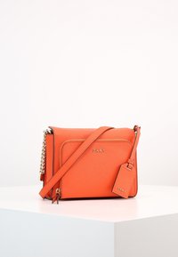Orange DKNY axelväska med texturfinish, guldfärgad hårdvara, avtagbar tag och en lång rem. Fyrkantig form med rena linjer.