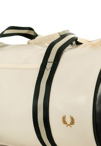 Borsa color crema con manico a righe verde scuro e crema. Realizzata in tessuto morbido, presenta un piccolo emblema dorato e una tasca con zip.