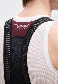 Bakside av en person som har på seg en hvit netting sykkeltrøye og svarte polstrede bib-shorts med "Castelli Performance Innovation Design"-logo.
