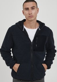 Navy blue fleece hoodie with a textured finish, contrasting black zippered chest pocket, full zipper, and side hand pockets.