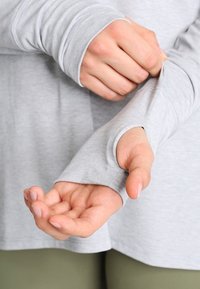Helles graues Langarmshirt mit Daumenlöchern. Der Stoff wirkt weich und elastisch, mit einer glatten Textur und dezenten Nahtdetails.