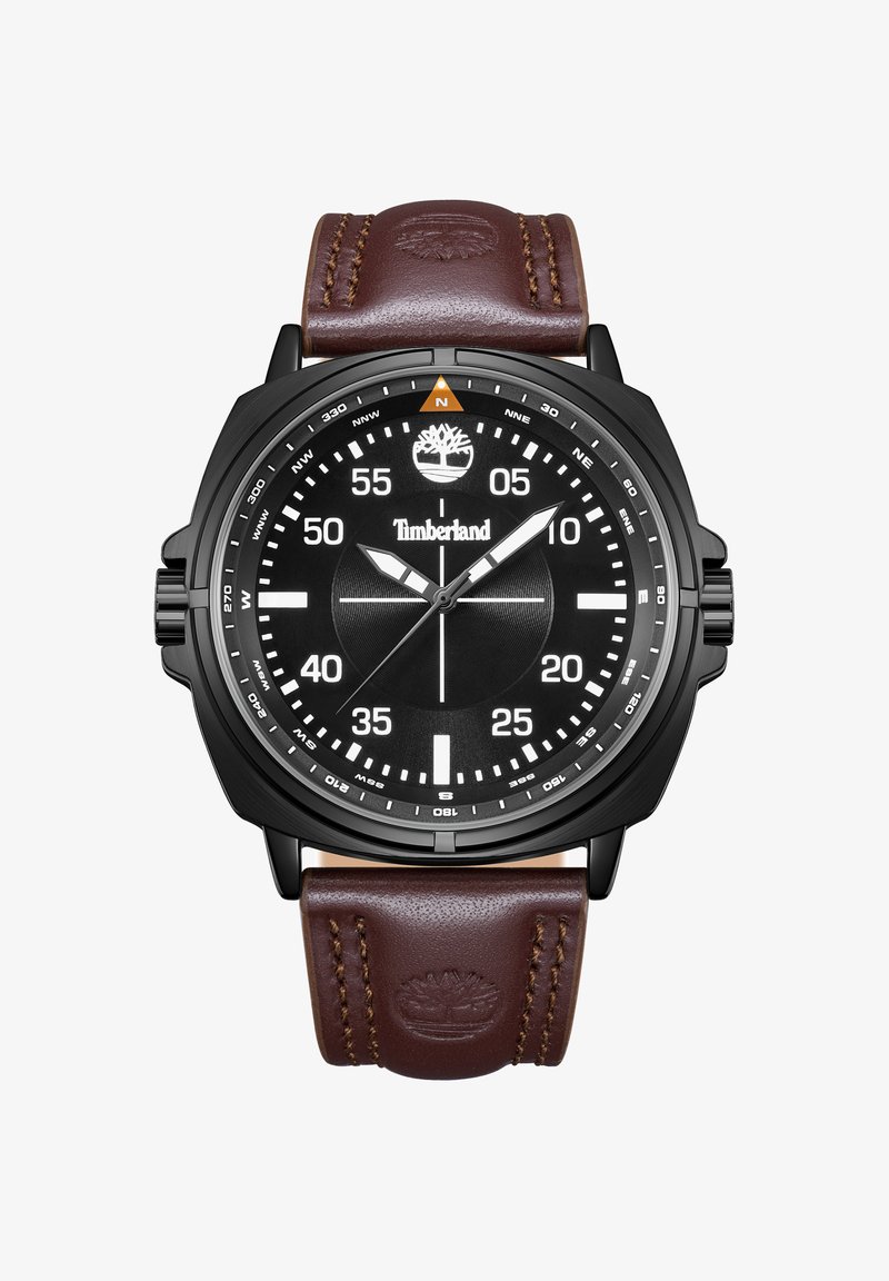 Rund sort Timberland-ur med hvide tal, kompasmarkeringer, tre visere og brun læderrem prydet med trælogo.