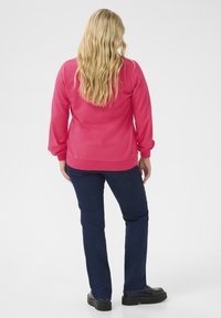 Fleece pulloveri kirkkaan vaaleanpunaisena pitkällä hihalla ja ribbailla hihoilla, yhdistetty tummansineihin farkkuihin ja mustiin platform-kengiin.