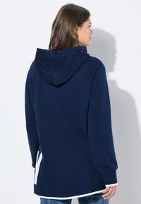 Sweat à capuche marine en tissu texturé, avec des poignets et un ourlet côtelés. Présente un motif blanc contrastant sur le bas.
