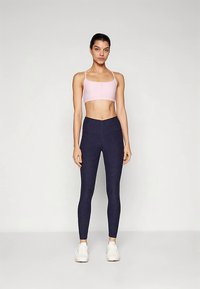 Šviesiai rožinės spalvos sportinė liemenėlė ir tamsiai mėlynos aukšto liemens tamprės, prigludusio dizaino, pagamintos iš tamprios medžiagos, turinčios subtilią tekstūrą be matomų raštų.