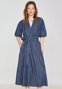 Abito di denim con scollatura a V profonda, maniche a sbuffo corte e vita legata, caratterizzato da una silhouette fluida e lunga fino alla caviglia in blu scuro.