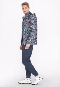 Giacca a stampa floreale con base blu navy, caratterizzata da fiori colorati. Abbinata a pantaloni blu navy e sneaker bianche con accenti neri.
