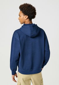 Granatowy hoodie wykonany z miękkiego materiału, z luźnym krojem, ściągaczami na mankietach oraz kangurzą kieszenią wszytą z przodu.