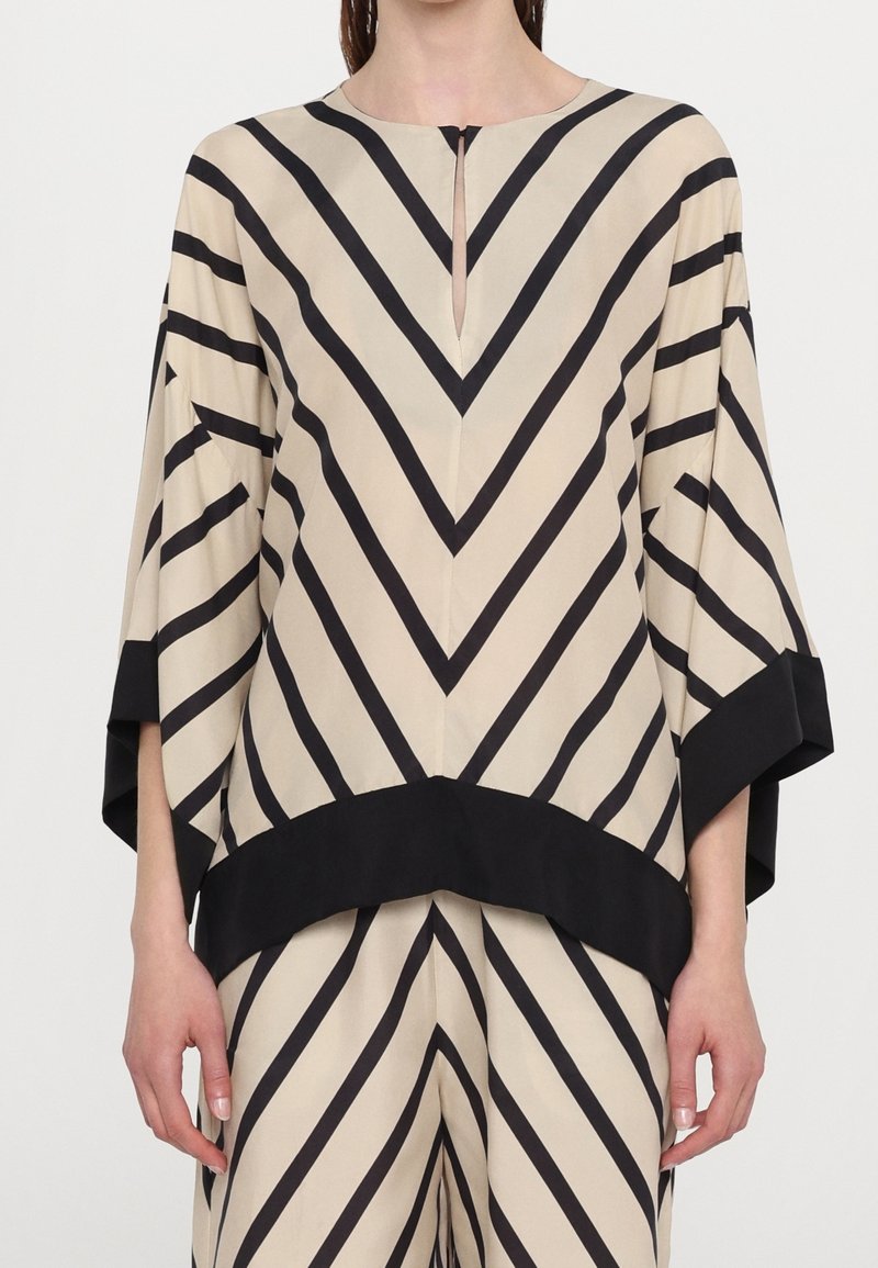 Ensemble ample beige composé d’un haut et d’un pantalon avec de larges rayures diagonales noires formant un motif chevron et une bordure noire aux manches et à l’ourlet.