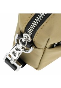 Beige nylon taske med en sølvfarvet lynlås, sorte accenter og en fremtrædende metalspænde med et 'B' design.