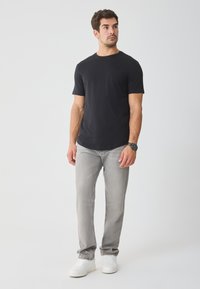 T-shirt preta de manga curta, material em algodão, gola redonda; combinado com calças de denim cinza claro e ténis brancos. Design simples, sem padrões.