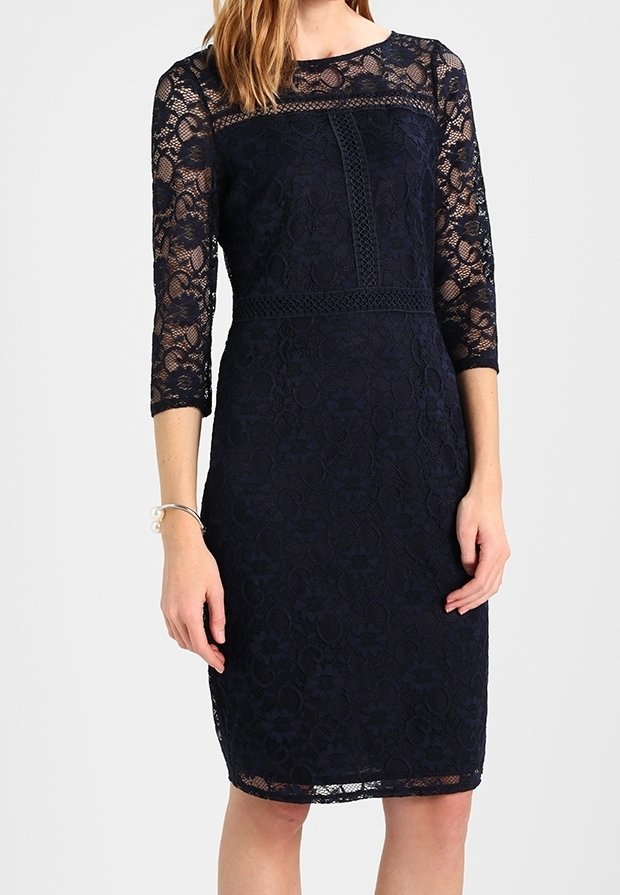 Femme portant une robe en dentelle bleu marine longueur genou avec des manches trois-quarts et un décolleté en dentelle transparente.
