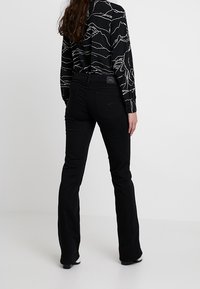 Jeans negros acampanados con una textura suave y una cintura ajustada, combinados con una camiseta de manga larga negra que presenta patrones de líneas de montaña en blanco.