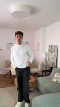 Fehér, hosszú ujjú ing és fekete nadrág, egy világos színű szobában áll, amelyben egy kerek felső lámpa, tükör és bézs székek találhatók.