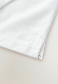 Valge puuvillane polo särk, millel on tekstureeritud kanga pind, tikitud krae ja väike, bordüüritud 'Clarks' logo hemil.