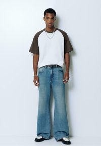 White and brown raglan t-shirt paired with wide-leg light blue denim jeans and black loafers with white accents. Accessories include layered chains.